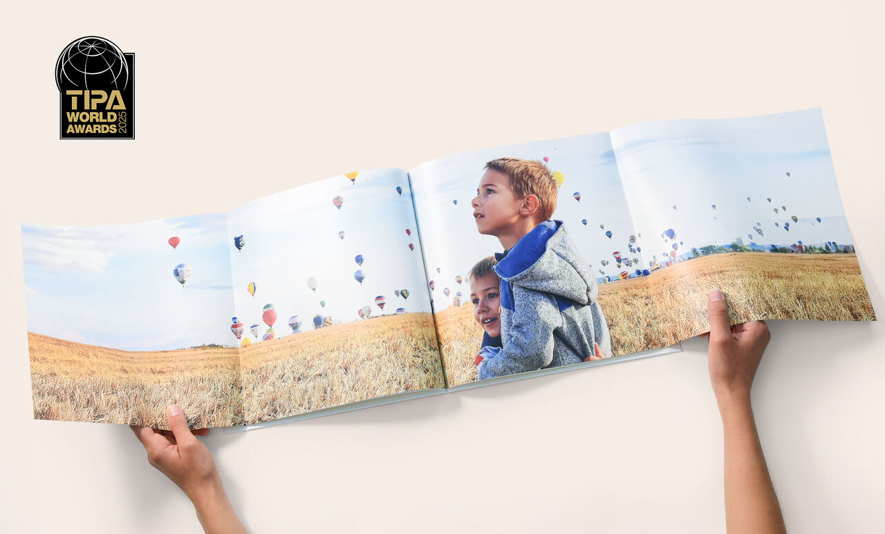 Un enfant tient un grand album photo avec des ballons dans un paysage.
