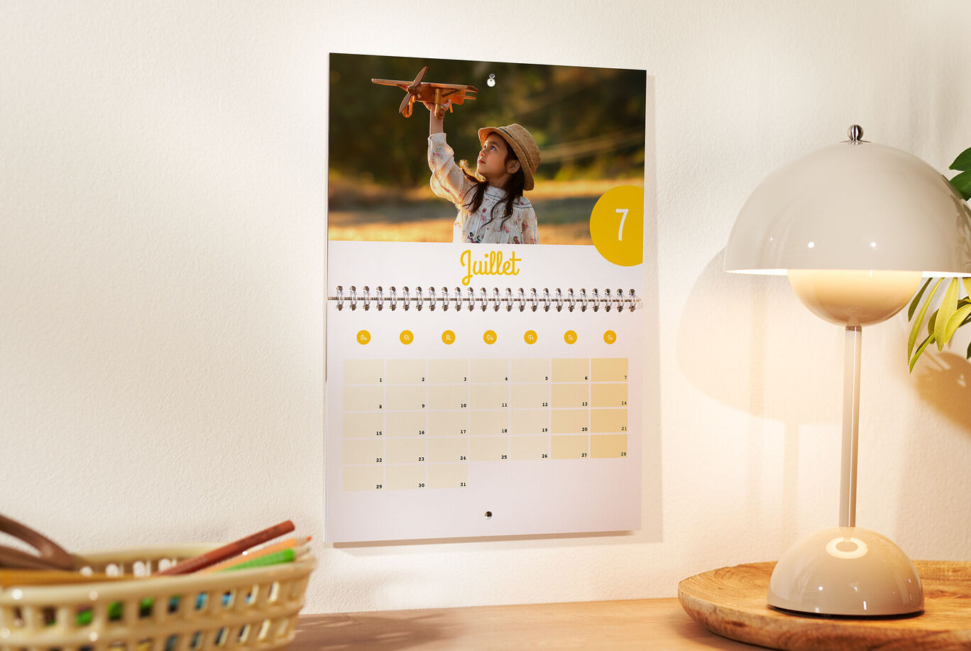 Un calendrier mural avec une photo d'un enfant jouant avec un avion en bois, marqué pour le mois de juillet