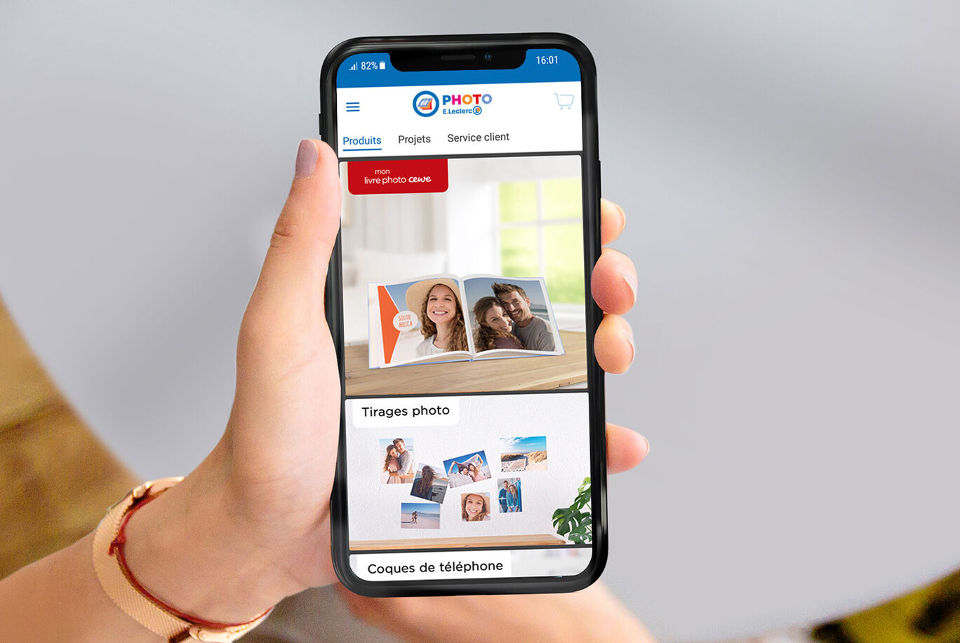 Une personne tient un smartphone montrant le site web de CEWE pour les livres photo.