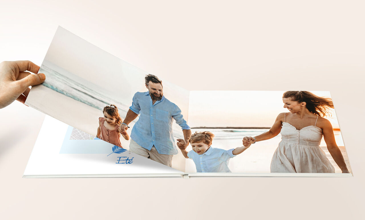 Une main feuillette un album photo CEWE avec des images d'une famille à la plage.