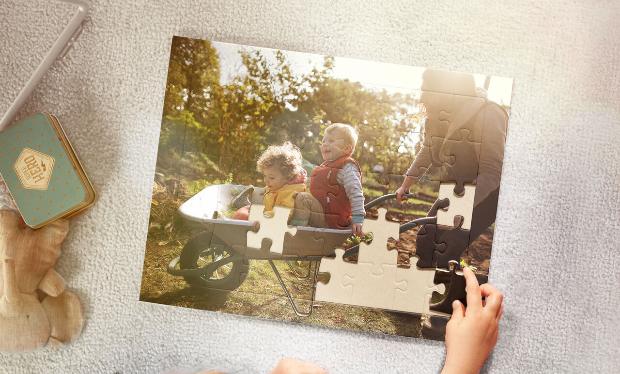 Deux enfants et un adulte faisant un puzzle en plein air, une brouette en arrière-plan.