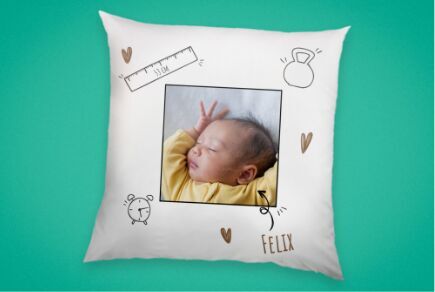 Un coussin joliment décoré avec une photo d'un bébé et des illustrations dessinées à la main, comme des cœurs et un mètre.