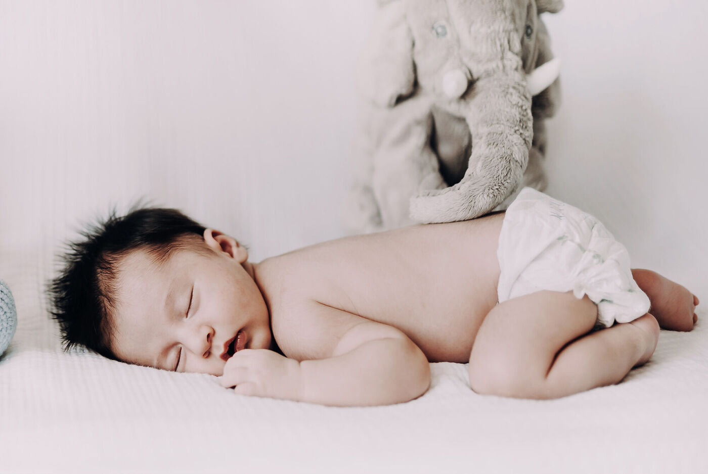 Un bébé dort paisiblement sur une couverture, entouré d'une peluche éléphant grise.