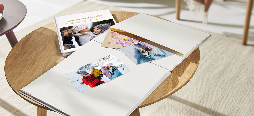 Table ouverte avec un CEWE ALBUM photo et une carte de vœux. L'album montre une photo de famille et un doux souvenir.