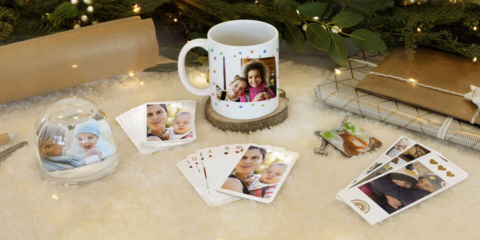 Différents produits CEWE avec des photos personnelles sur une table, dont une tasse et des cartes de jeu.