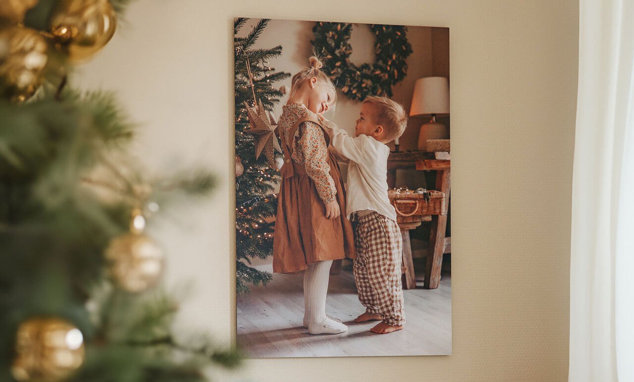 Deux enfants décorent un sapin de Noël dans une pièce cosy. L'un porte une robe brune, l'autre une blouse blanche avec un pantalon à pois.