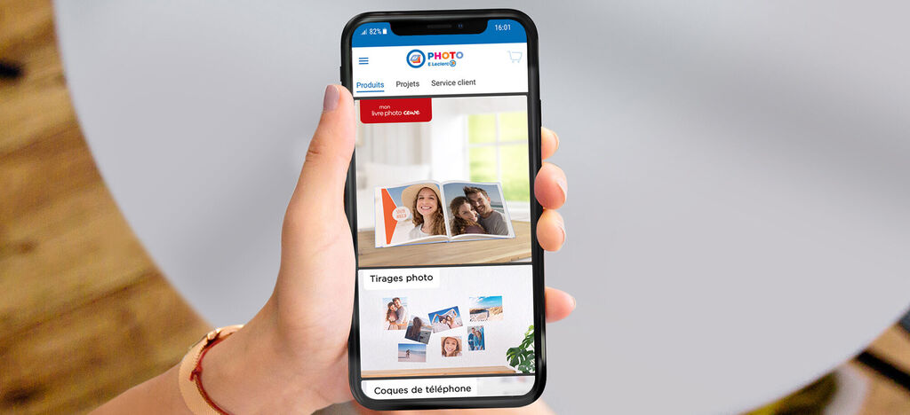 Une main avec un smartphone montre le livre photo CEWE sur le site web.