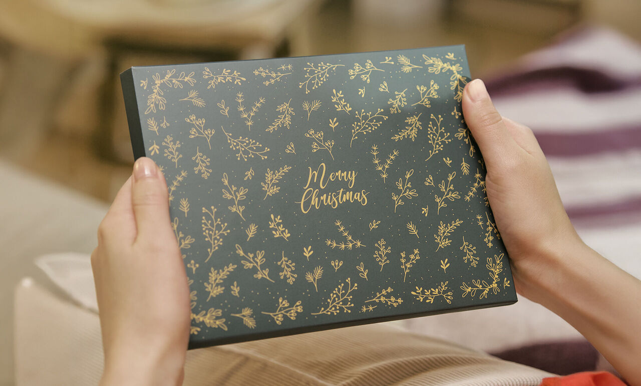 Une personne tient une boîte de Noël avec des motifs dorés.