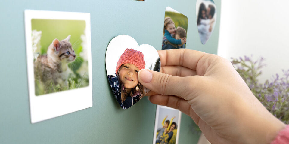 Une main fixe une photo en forme de cœur sur un mur avec diverses images.