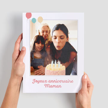 Une personne tient un album photo avec une fête d'anniversaire. Des bougies sont sur le gâteau.