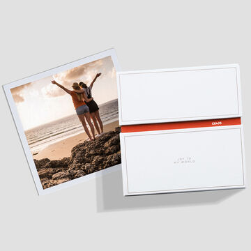 Deux amies se tiennent sur la plage et profitent du moment. Elles étendent les bras pendant que les vagues roulent doucement sur le rivage. CEWE PHOTOBOOK est visible.