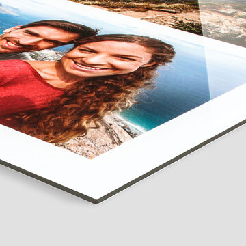 Un couple heureux sourit à la caméra, l'océan scintille en arrière-plan. Album photo CEWE.