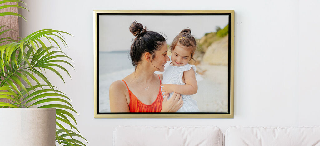 Une mère tient son petit enfant sur la plage, tous deux sourient et profitent du soleil.