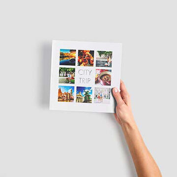 Une main tient un album CEWE avec des photos d'un voyage en ville. La couverture montre des photos et le titre 'CITY TRIP'.