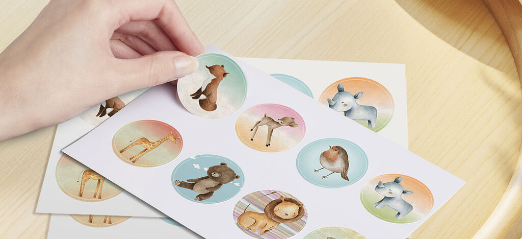 Deux piles de feuilles avec des autocollants d'animaux ronds, une main tient un autocollant.