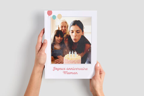 Une personne tient un album photo CEWE d'une fête d'anniversaire. On voit le gâteau et les bougies. C'est un moment chaleureux.