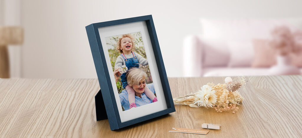 Une photo de famille dans un cadre sur une table en bois, avec une fleur et un petit morceau de bois à côté.