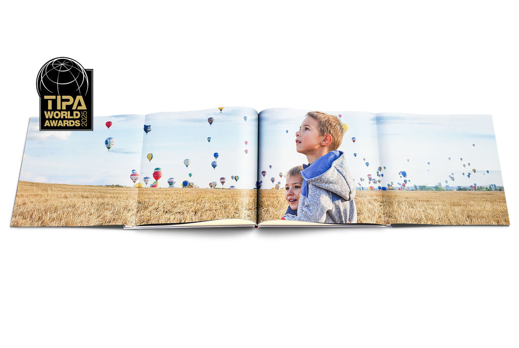Un livre photo ouvert avec un enfant dans un paysage, entouré de montgolfières colorées sous un ciel atmosphérique