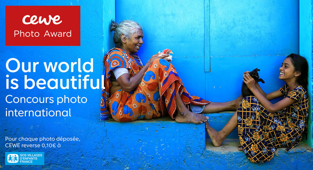 Deux femmes en robes colorées assises devant un mur bleu. L'une tient un animal noir, diffusant joie et communauté.