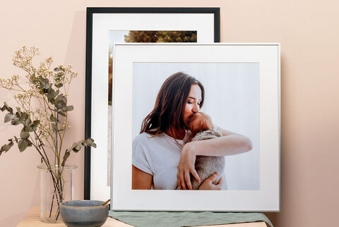 Une personne tenant amoureusement un bébé, entourée de photos encadrées et de plantes.