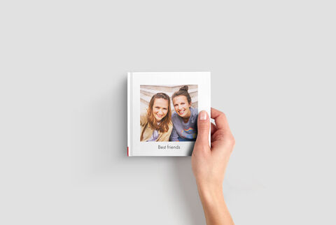 Une main tient un livre photo CEWE intitulé 'Meilleurs amis'.