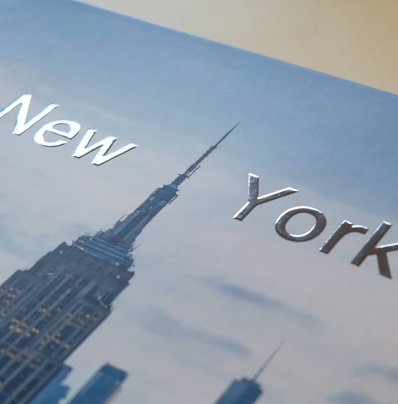 Gros plan sur la couverture d'un livre photo avec l'inscription 'New York' et le sommet de l'Empire State Building en arrière-plan.