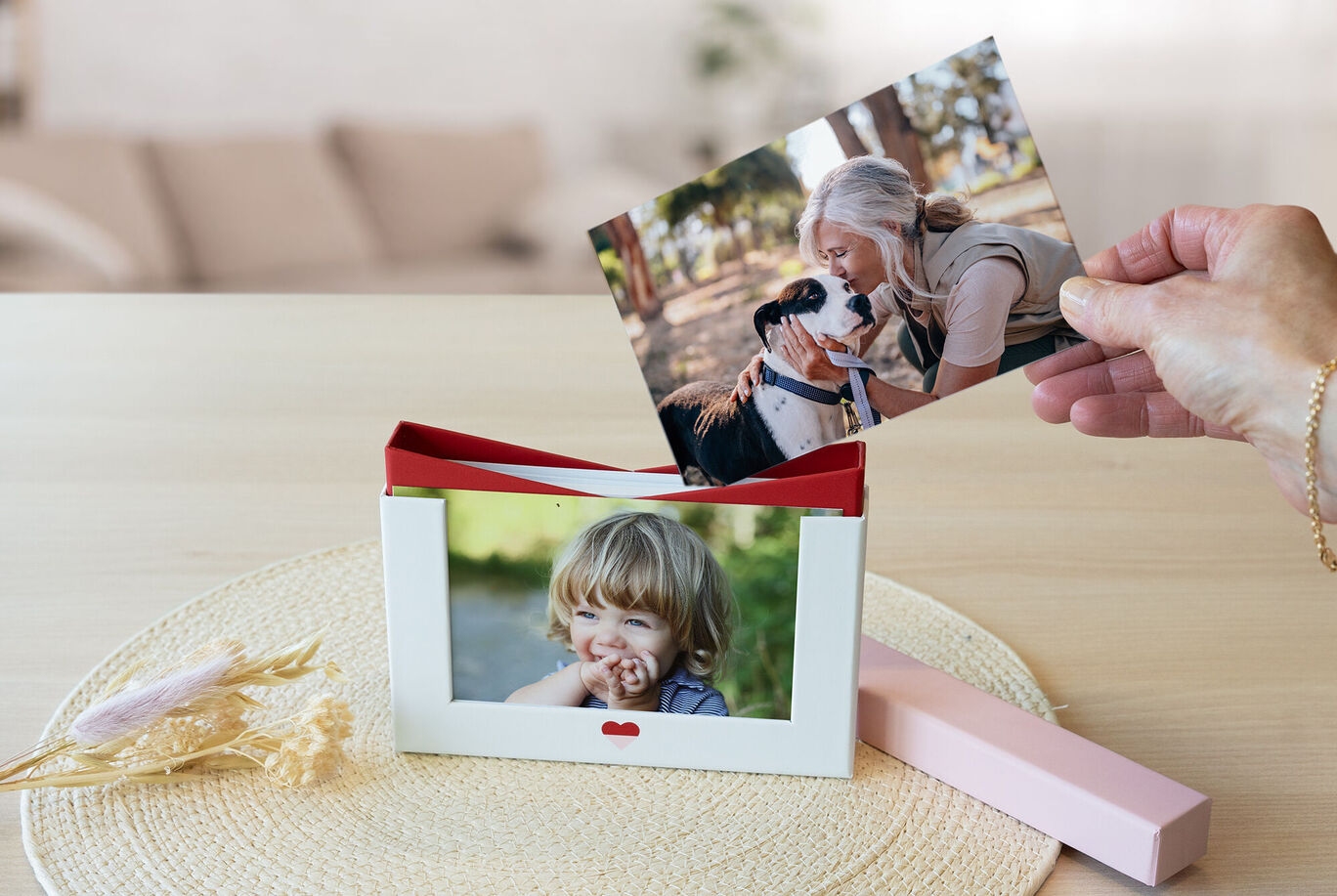 Une main tient une photo tandis qu'une autre photo est dans un cadre décoratif sur une table.