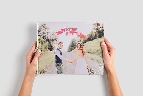 Un couple tient un CEWE PhotoBook avec leur photo de mariage sur la couverture.