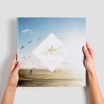 Une personne tient un CEWE Photo Book intitulé "Explorez le Monde" devant un fond clair