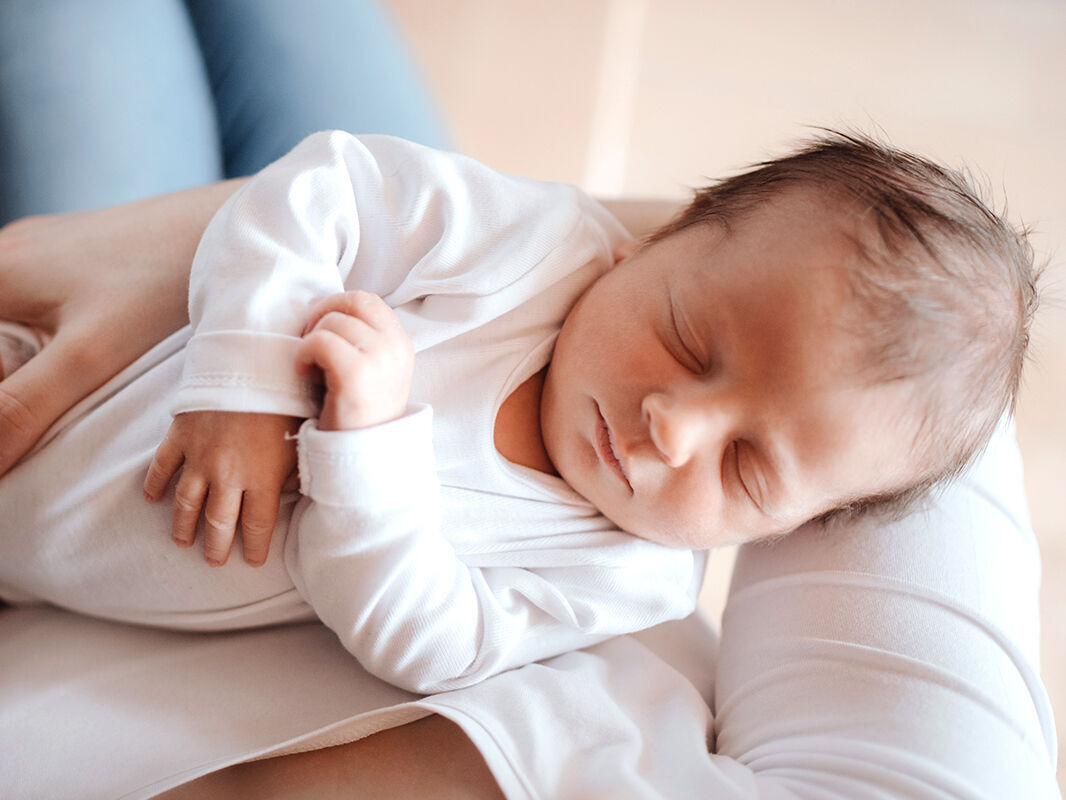 Un bébé en robe blanche est tendrement tenu.