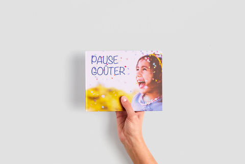Une personne tient un album photo CEWE titré 'Pause Gouter'.