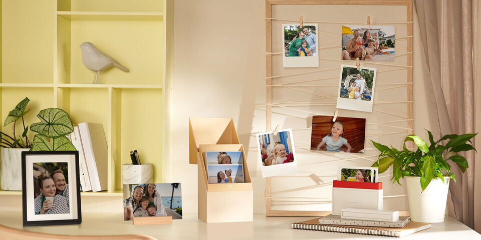 Une pièce lumineuse avec un mur photo créatif. Des cadres photo sont sur une table avec des photos de proches.