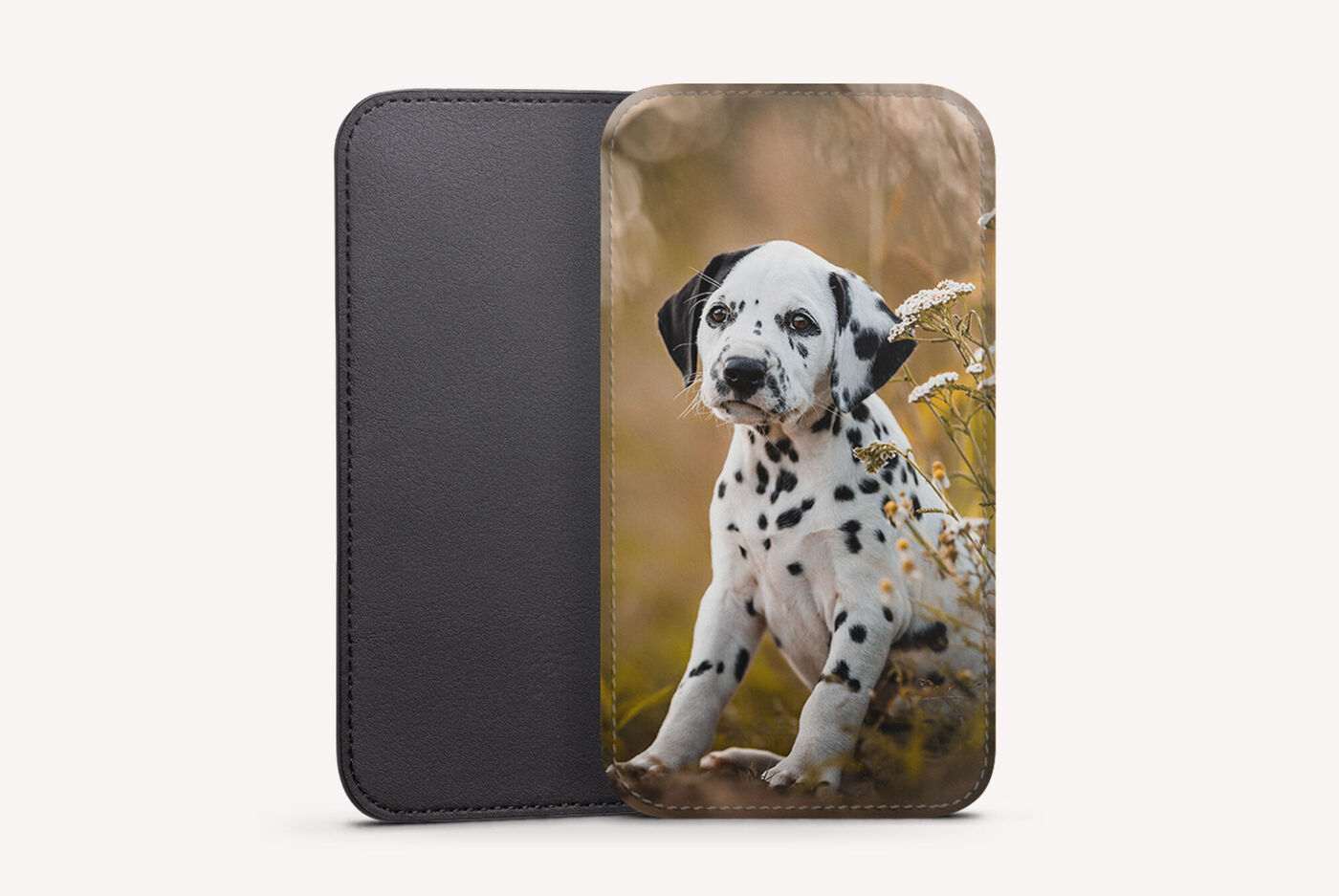 Un beau chiot dalmatien est assis dans des herbes hautes avec des fleurs.