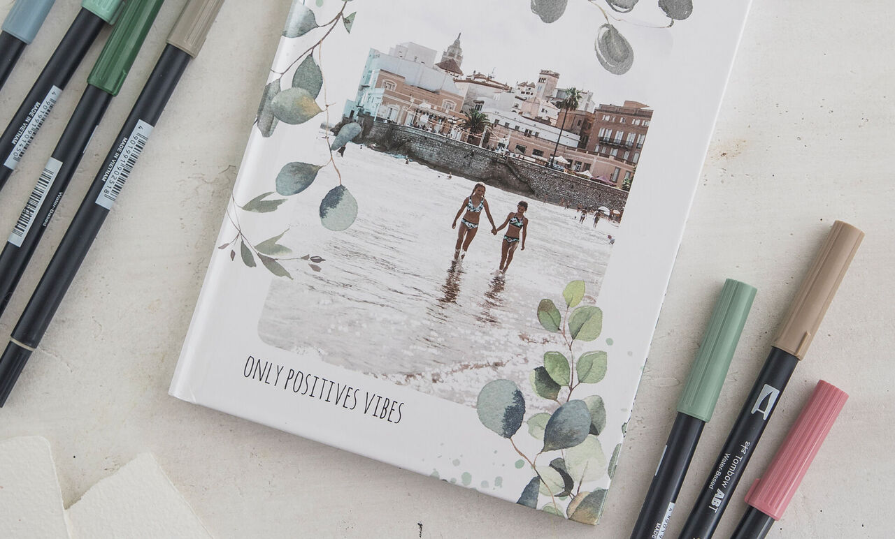 Cahier rigide décoré de motifs de feuilles, photo de plage avec deux personnes et inscription Only positives vibes.