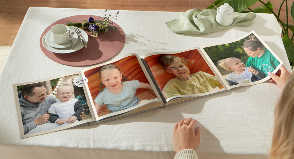 Une personne regarde un livre photo ouvert sur une table avec des fleurs et une tasse.