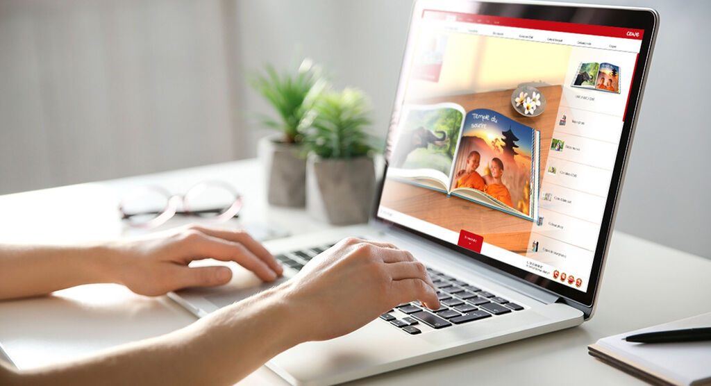 Une personne travaille sur un ordinateur portable, un album CEWE affiché à l'écran.