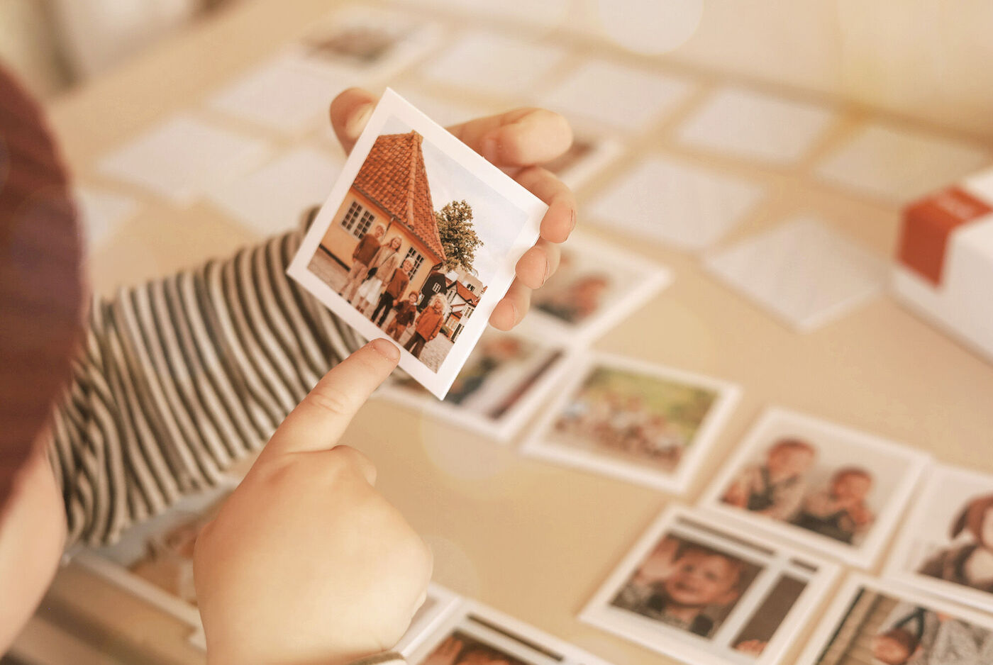 Un enfant montre une photo d'une maison avec un toit rouge. D'autres images sont sur une table en arrière-plan.