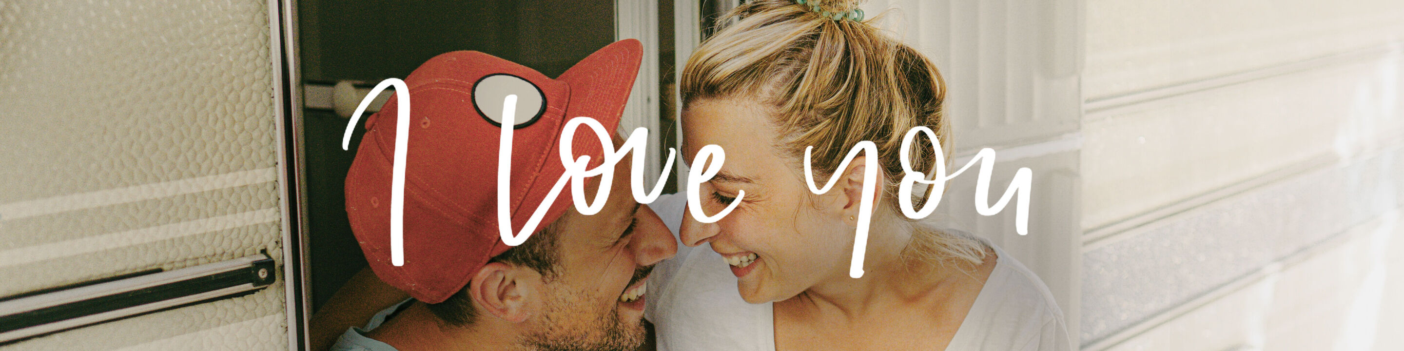 Une jeune personne avec un bonnet rouge embrassant une autre personne sur la joue, mur clair en arrière-plan