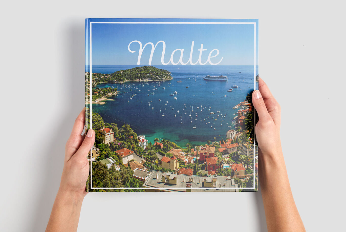 Des mains tiennent un album photo intitulé Malte sur une table devant une belle vue côtière.