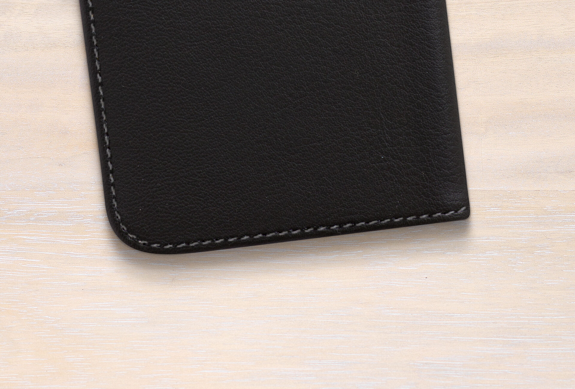 Surface en bois clair avec un portefeuille en cuir noir dans le coin inférieur gauche.