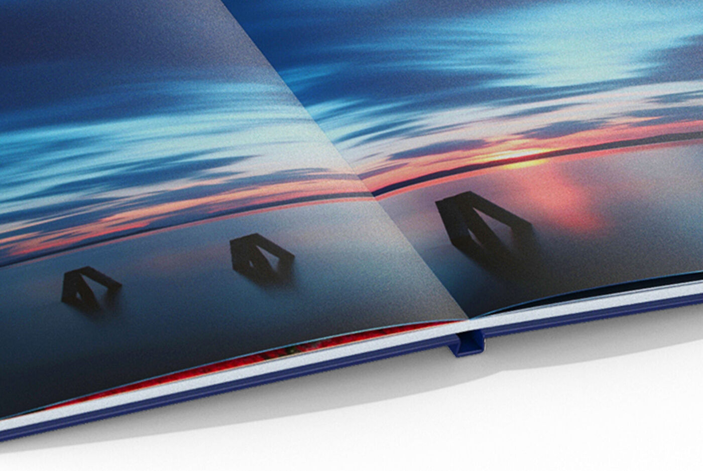 Livre photo ouvert montre un paysage coloré au-dessus d'une eau tranquille. Les pages sont légèrement ondulées avec des couleurs vives.