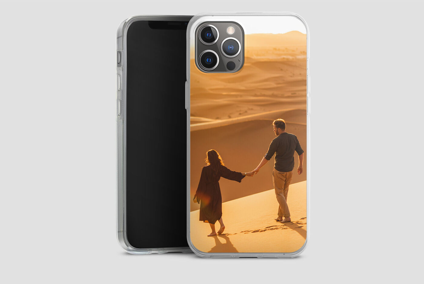 Un couple se promène main dans la main sur une dune de sable au coucher du soleil.