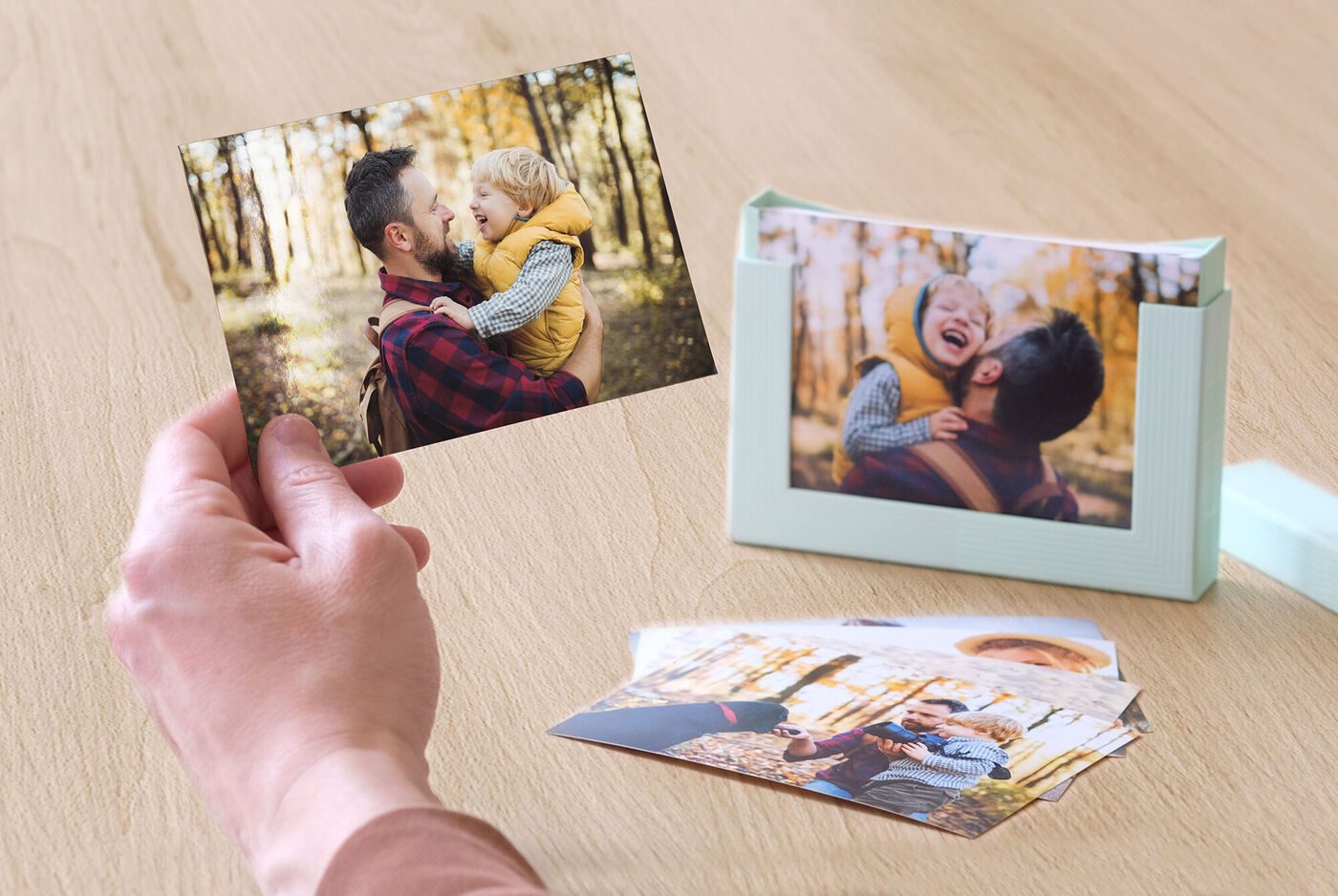 Une personne tient une photo d'une autre personne dans la nature, entourée de feuilles colorées.