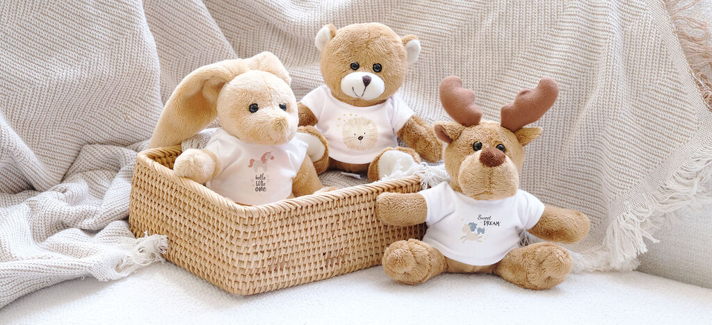 Trois peluches adorables dans un panier sur un doux plaid. Un lapin, un ours et un renne expriment de la joie.