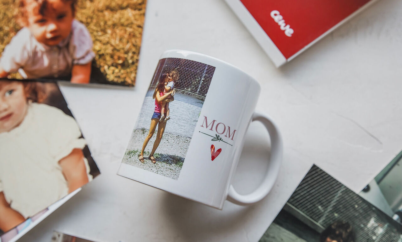 Tasse blanche "Mom" avec portrait imprimé et petit cœur rouge, posée parmi plusieurs photos.