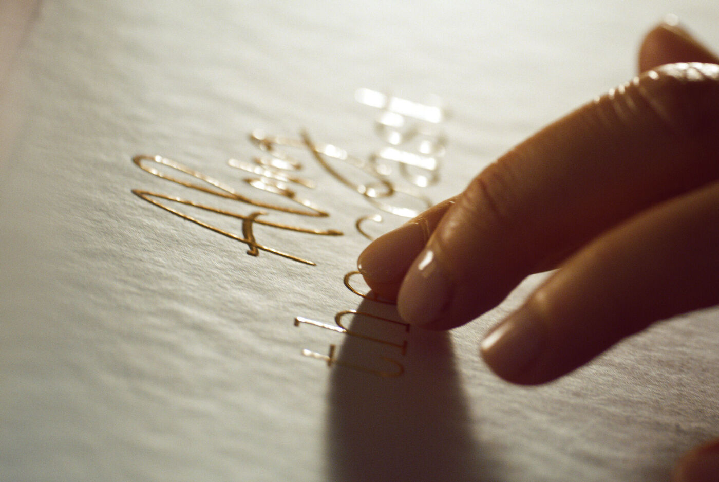 Une main touche une écriture dorée sur papier blanc.