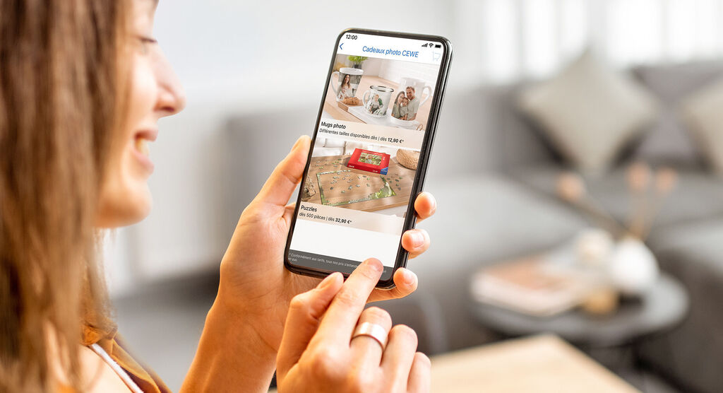 Une personne tient un smartphone et fait défiler une application pour concevoir des produits CEWE.