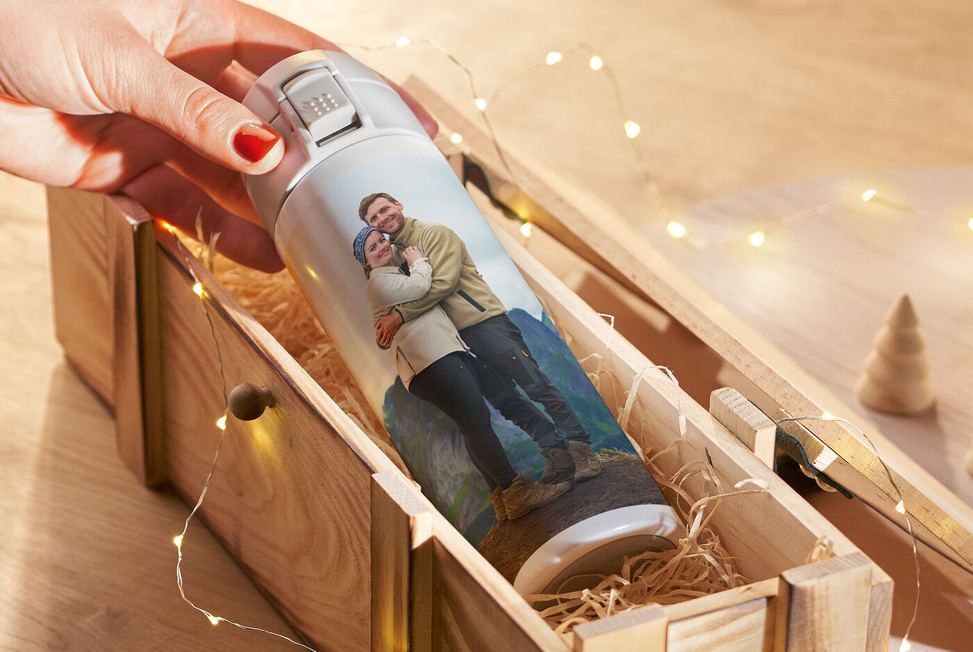 Une personne tient une thermos personnalisée avec une photo d'un couple, dans une boîte en bois.