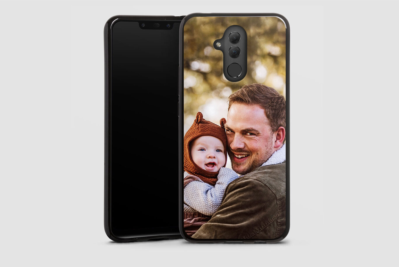 Un père tient son enfant dans ses bras, avec un smartphone en arrière-plan.