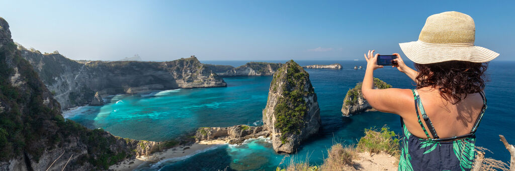 Une personne photographie avec un smartphone le paysage côtier impressionnant avec des falaises et une eau turquoise à Nusa Penida.